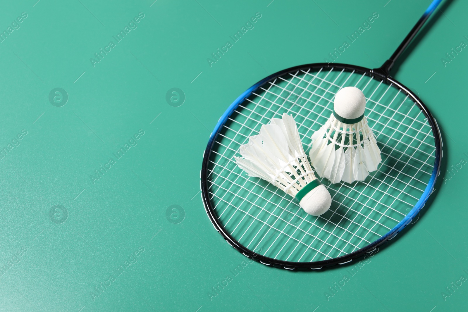 Photo of Feather badminton shuttlecocks and racket on green background. Space for text