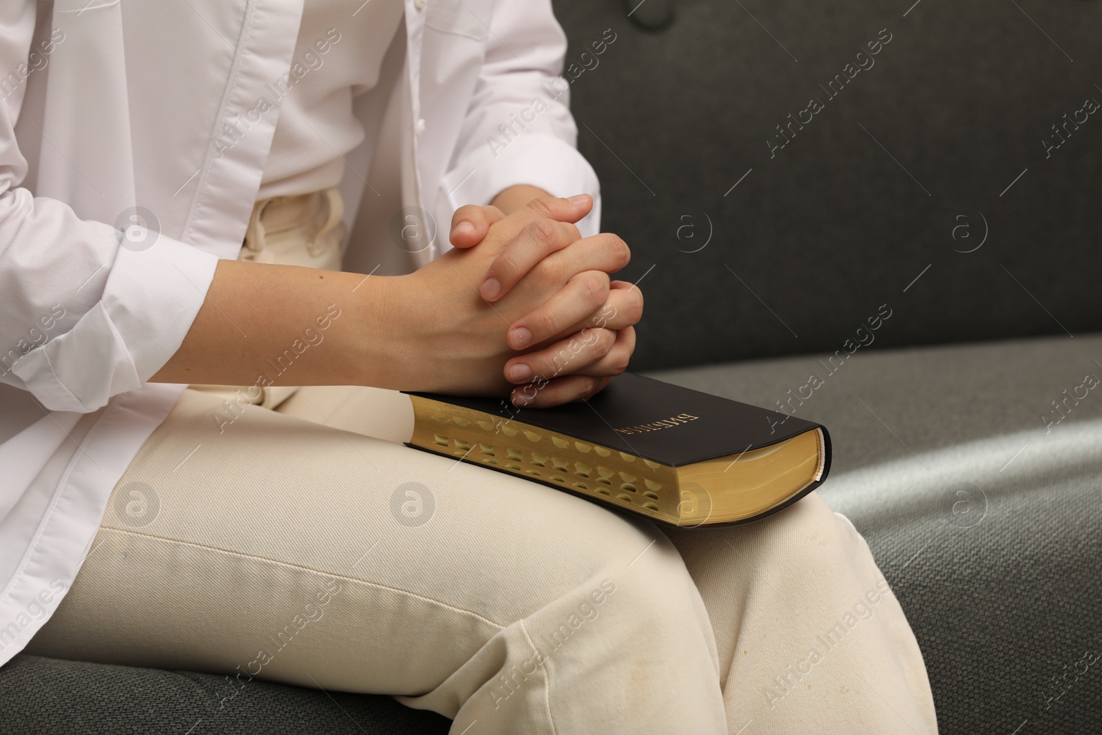 Photo of Religious woman praying over Bible indoors, closeup