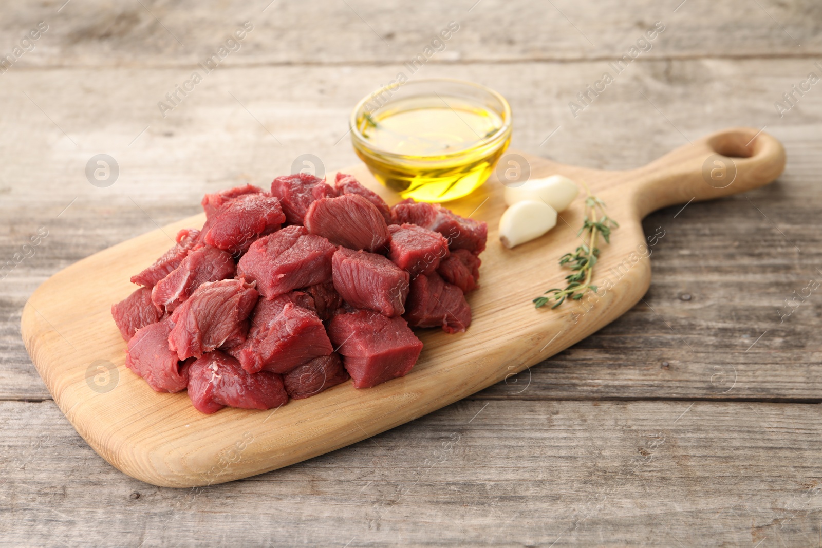 Photo of Pieces of raw beef meat, oil and garlic on wooden table