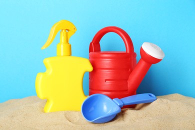 Suntan product and plastic beach toys on sand against light blue background