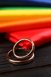 Photo of Rainbow LGBT flag and wedding rings on black wooden background