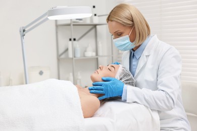 Dermatologist examining patient`s face under lamp in clinic