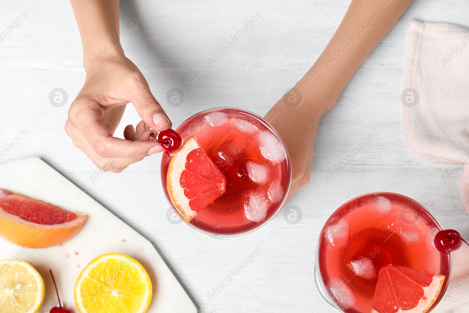 Photo of Woman decorating freshly made cocktail with cherry at white wooden table, top view