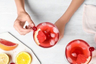 Woman decorating freshly made cocktail with cherry at white wooden table, top view