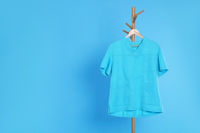 Turquoise medical uniform hanging on rack against light blue background. Space for text