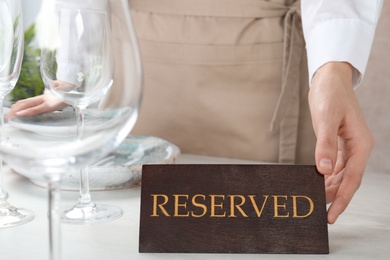 Photo of Waiter setting RESERVED sign on restaurant table, closeup