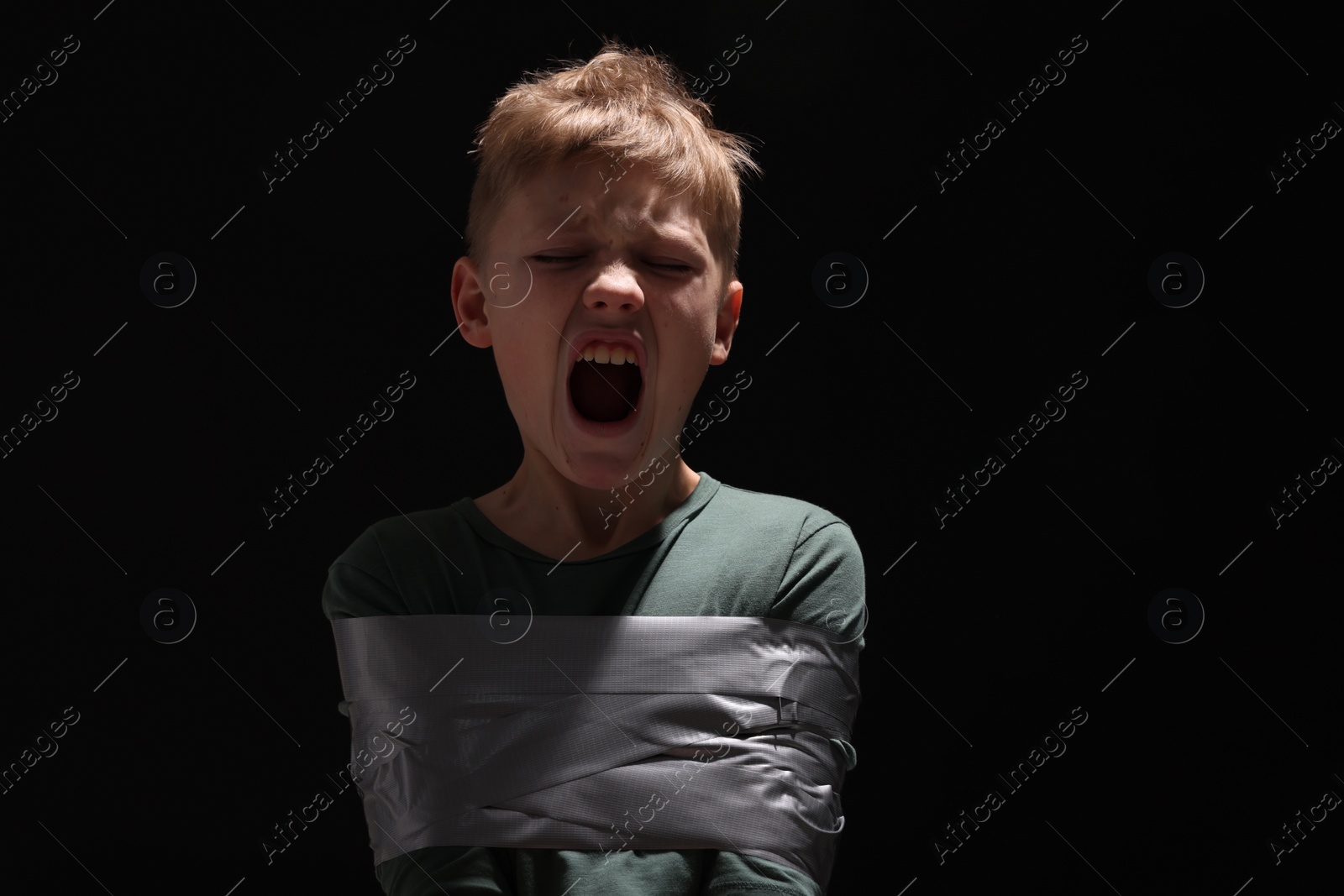 Photo of Scarred little boy tied up and taken hostage on dark background. Space for text