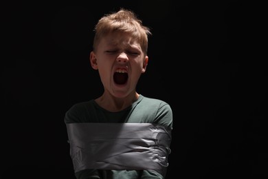Scarred little boy tied up and taken hostage on dark background. Space for text