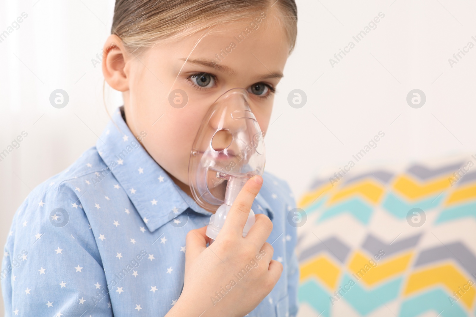 Photo of Sick little girl using nebulizer for inhalation indoors