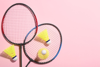 Photo of Badminton rackets and shuttlecocks on pink background, flat lay. Space for text