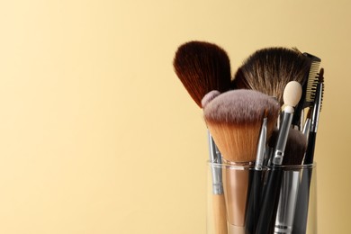 Photo of Set of professional makeup brushes on beige background, closeup. Space for text