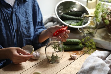 Photo of Woman putting pepper into jar in kitchen, closeup