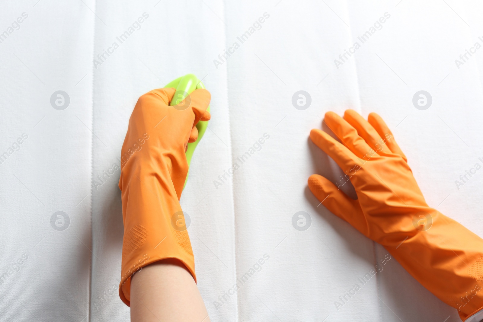 Photo of Woman in orange gloves cleaning white mattress with brush, top view