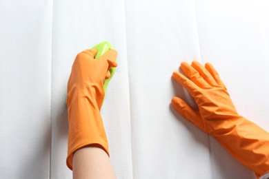 Photo of Woman in orange gloves cleaning white mattress with brush, top view