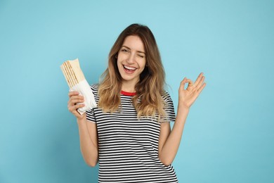 Young woman with delicious shawarma on turquoise background