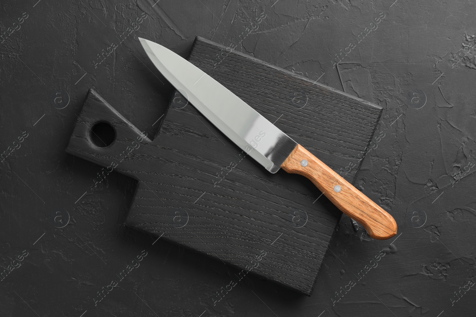 Photo of One sharp knife and board on dark textured table, top view