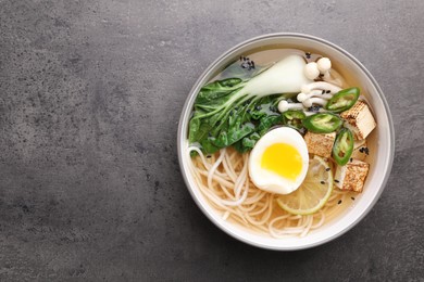 Bowl of vegetarian ramen on grey table, top view. Space for text