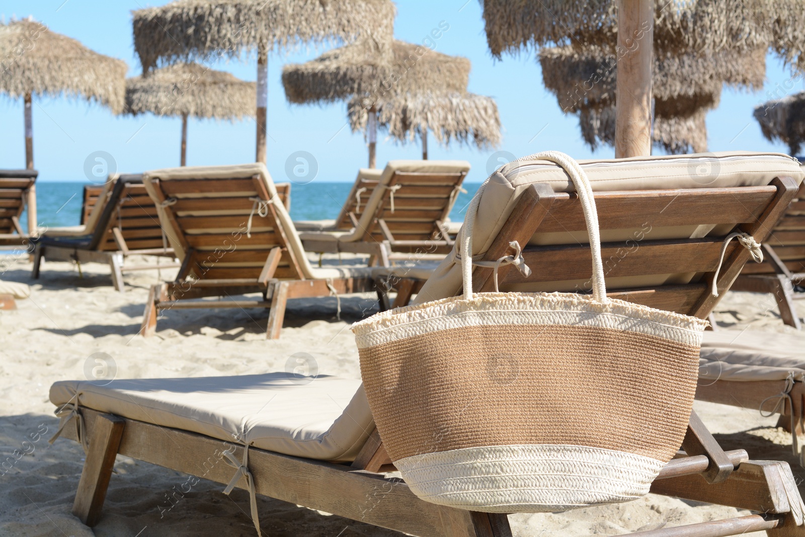 Photo of Straw bag on wooden sunbed near sea. Beach accessory