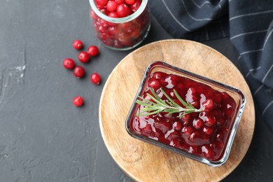 Photo of Tasty cranberry sauce in bowl and glass jar with fresh berries on gray textured table, flat lay. Space for text