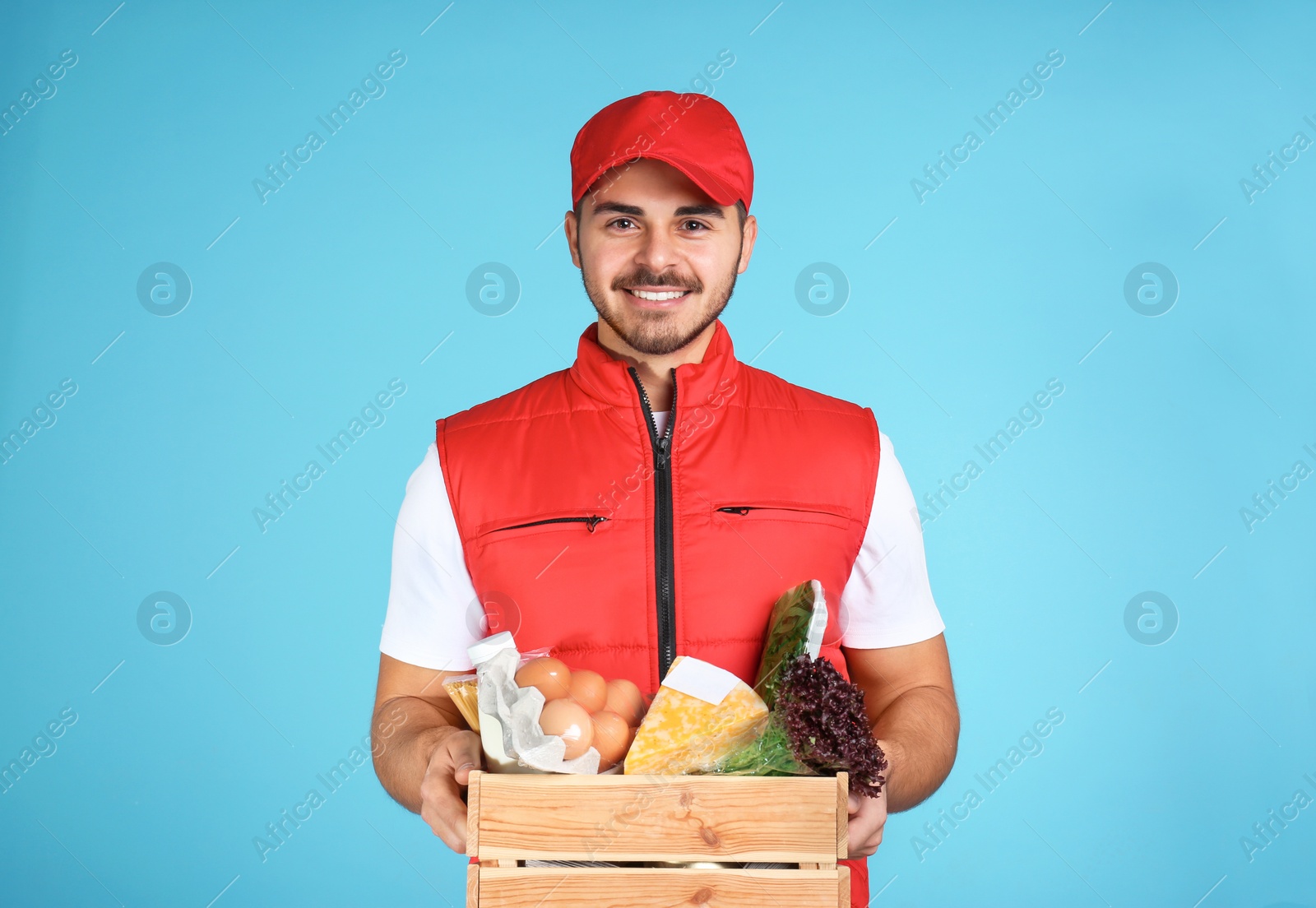 Photo of Young man holding wooden crate with products on color background. Food delivery service