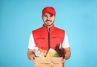 Young man holding wooden crate with products on color background. Food delivery service