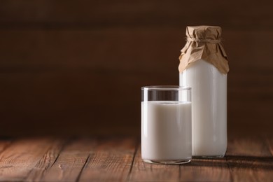 Tasty fresh milk in bottle and glass on wooden table, space for text