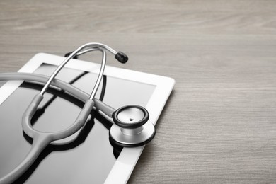 Photo of Computer tablet with stethoscope on wooden table, closeup. Space for text
