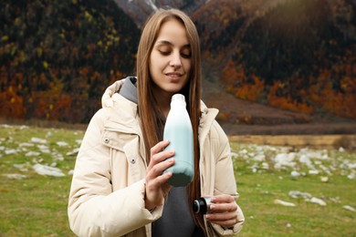 Photo of Woman holding thermo bottle with drink and cap in mountains