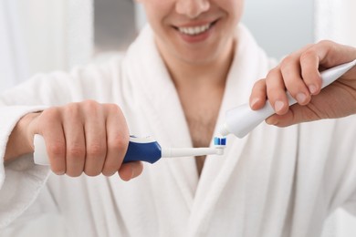 Photo of Man squeezing toothpaste from tube onto electric toothbrush indoors, closeup