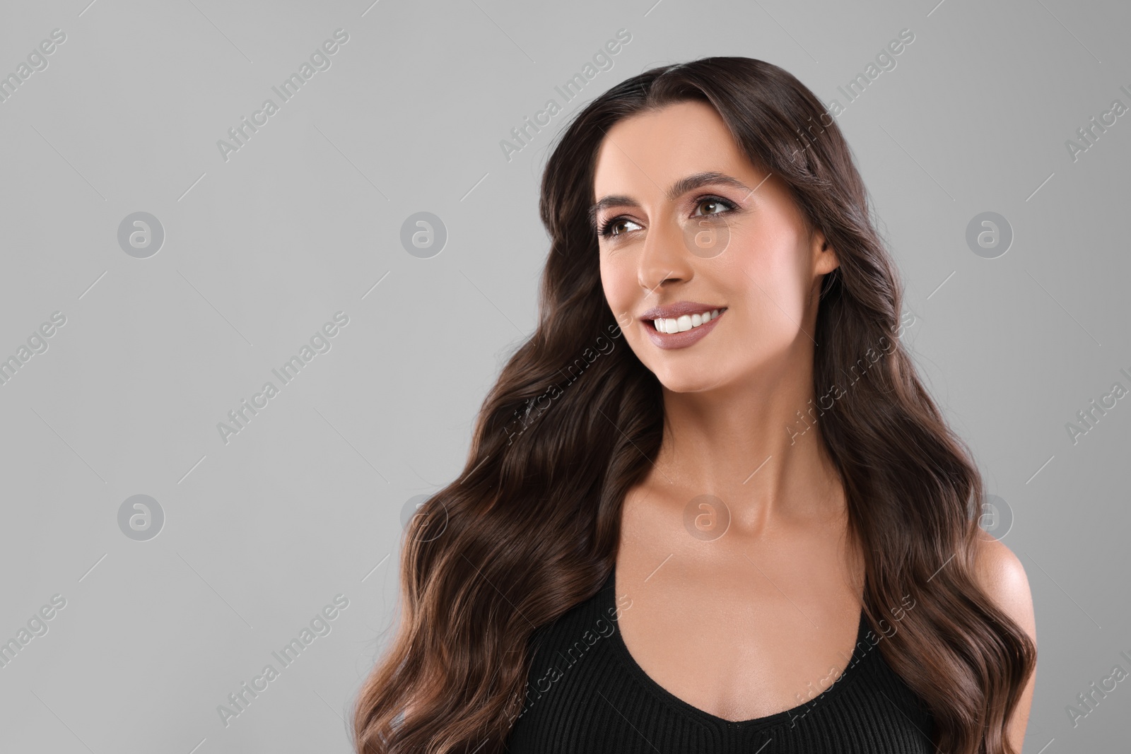 Photo of Hair styling. Beautiful woman with wavy long hair on grey background, space for text