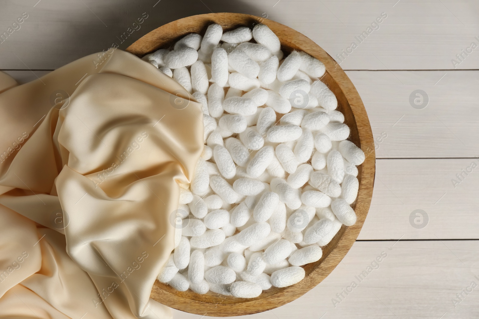 Photo of Cocoons with bowl and silk fabric on white wooden table, flat lay