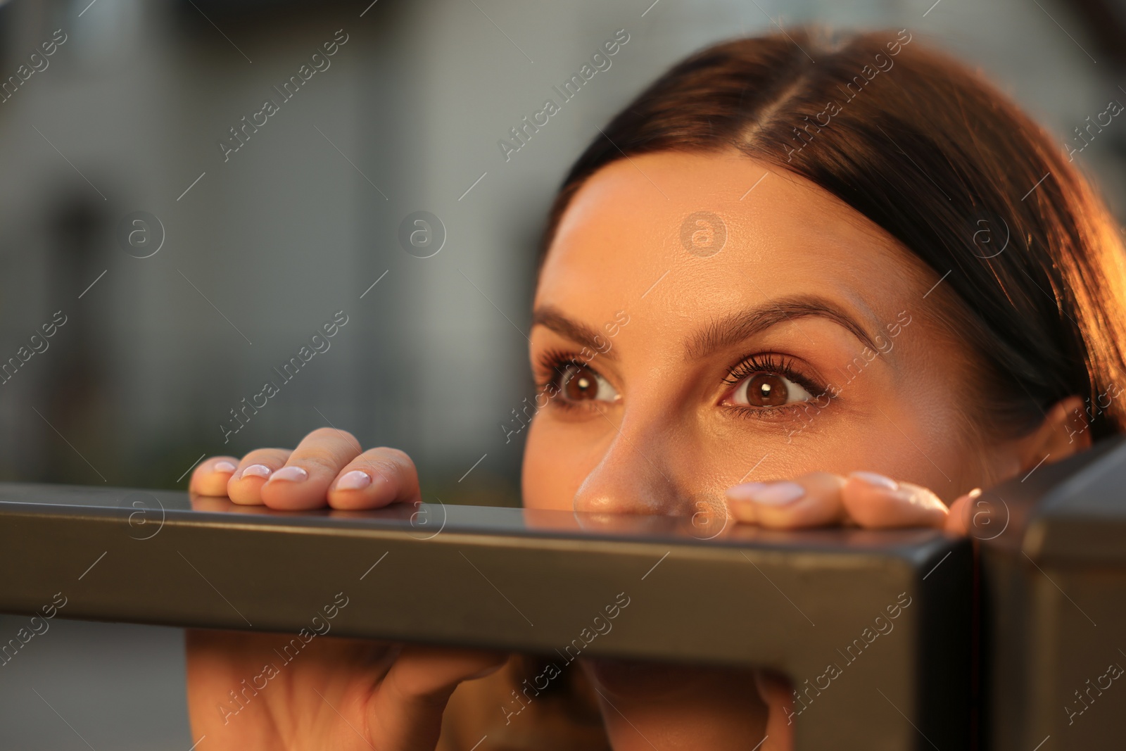 Photo of Concept of private life. Curious young woman spying on neighbours over fence outdoors, closeup