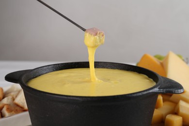 Photo of Dipping piece of ham into fondue pot with tasty melted cheese at table against gray background, closeup