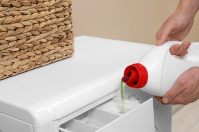 Photo of Man pouring fabric softener from bottle into washing machine indoors, closeup