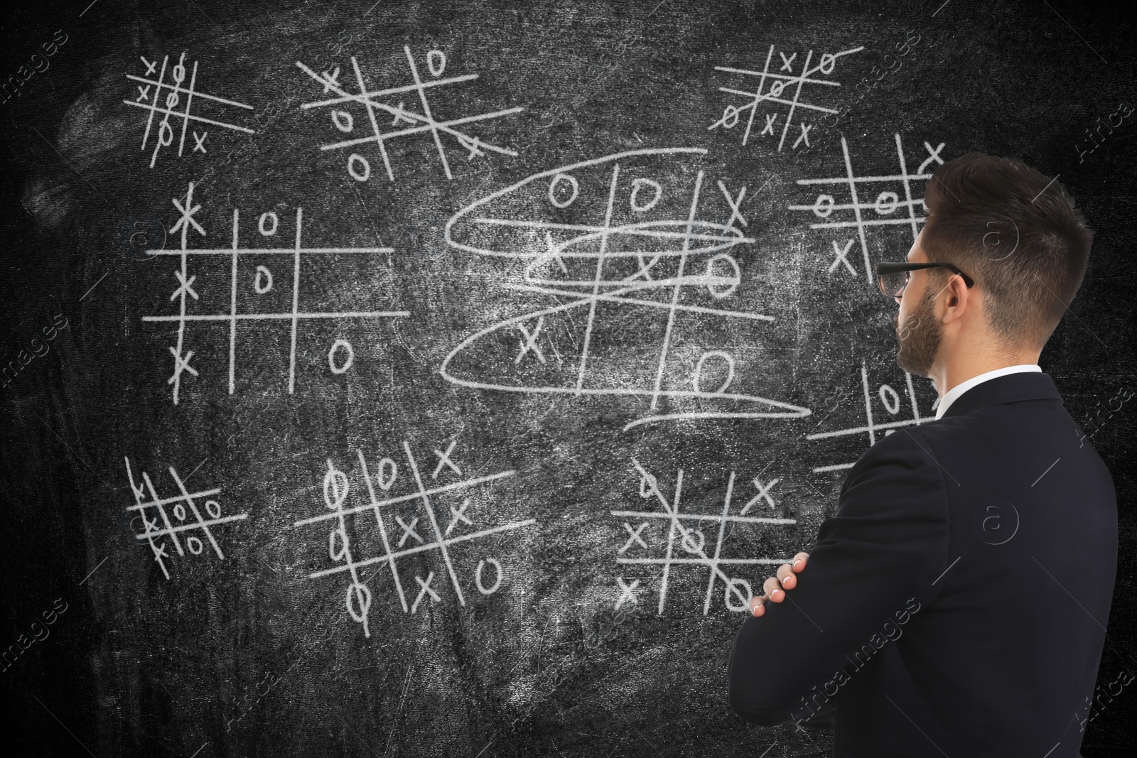 Image of Young businessman in elegant suit near blackboard with drawn tic tac toe game 