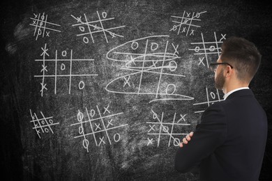 Young businessman in elegant suit near blackboard with drawn tic tac toe game 
