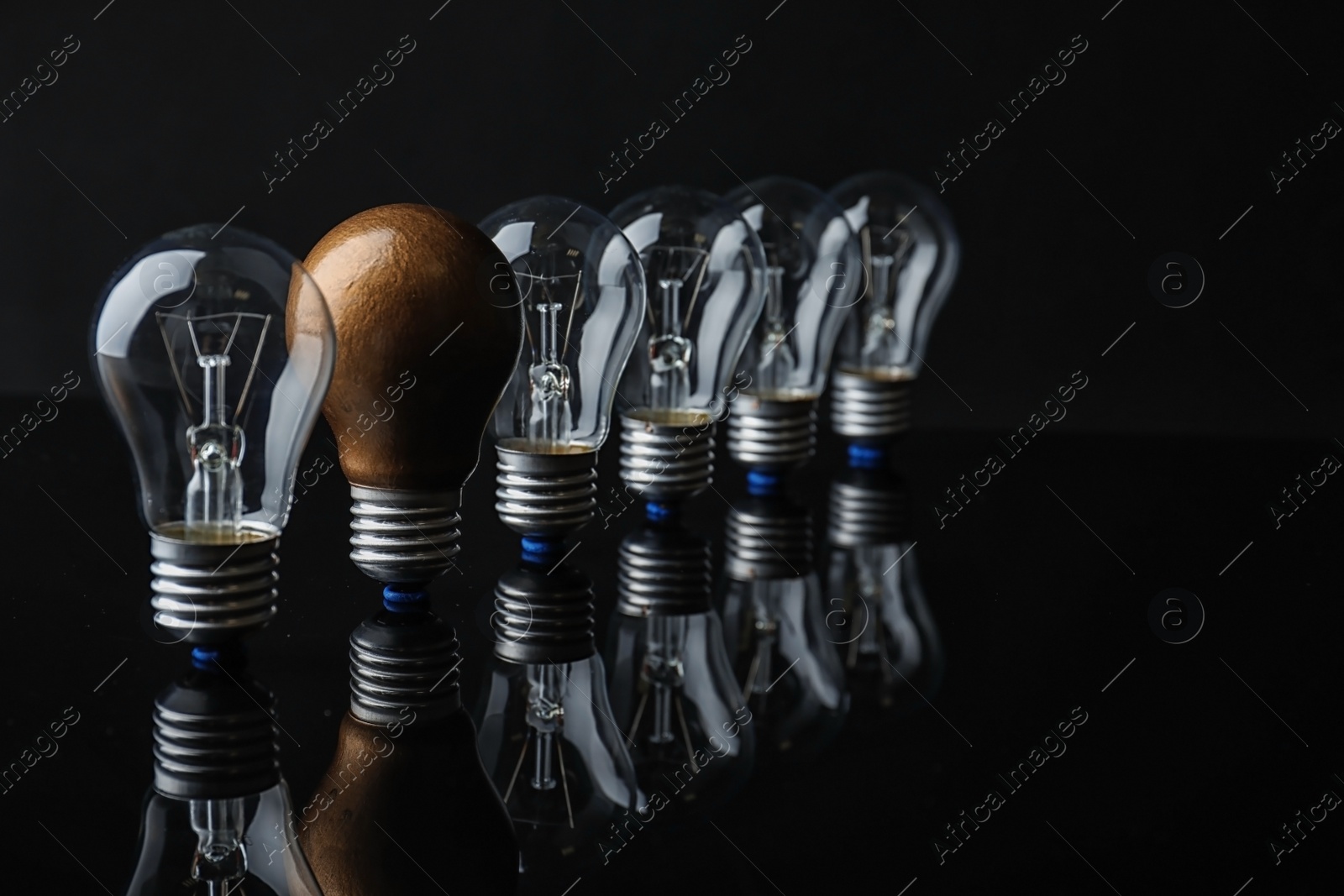 Photo of One different light bulb among others on black background