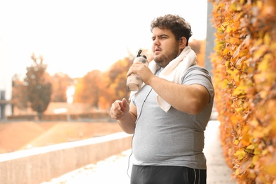 Photo of Young overweight man with towel and bottle of water in park
