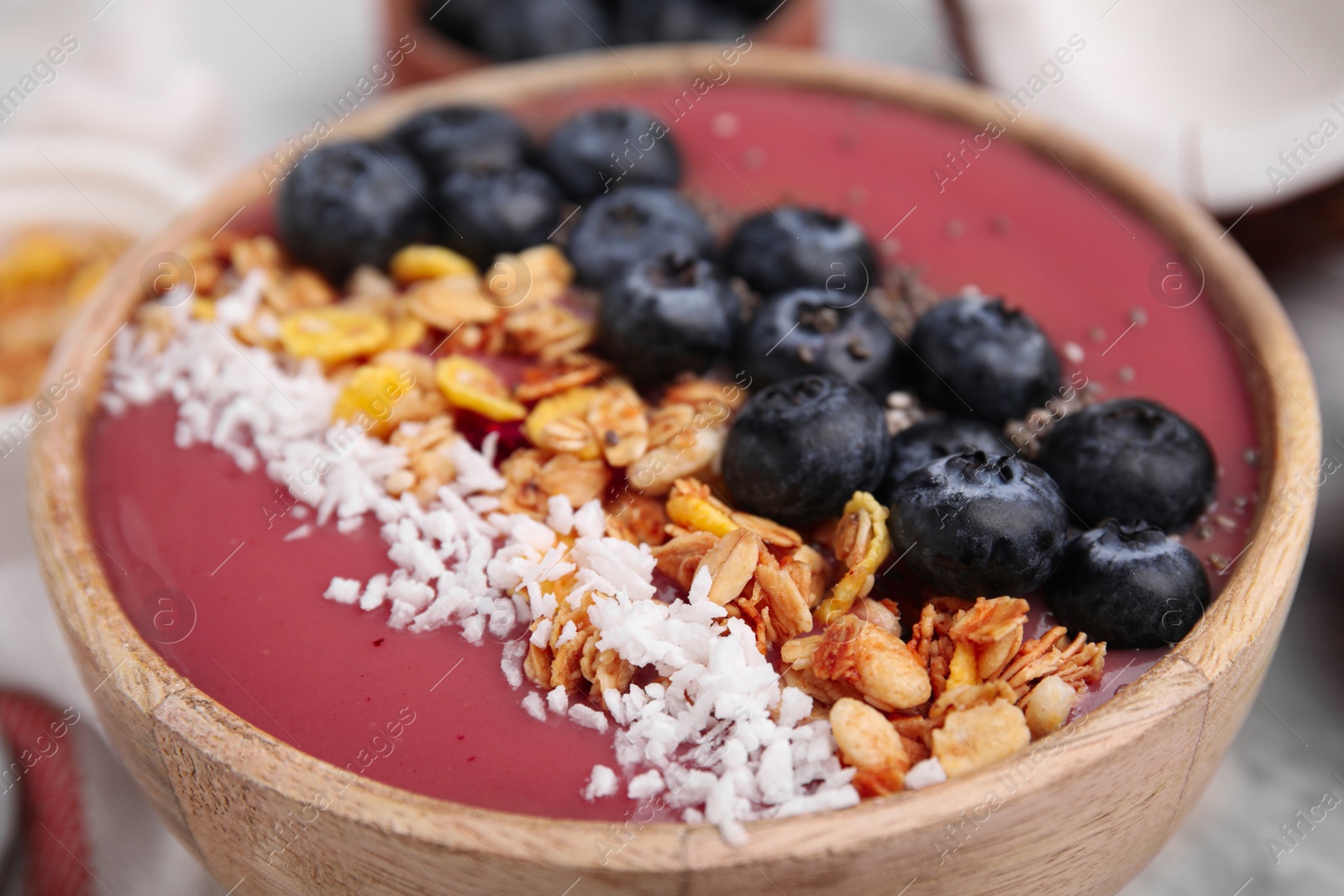 Photo of Bowl of delicious fruit smoothie with fresh blueberries, granola and coconut flakes on white marble table, closeup