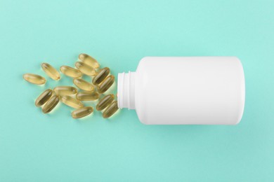 Bottle and vitamin capsules on turquoise background, top view