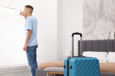 Photo of Guest looking through blinds in stylish hotel room, focus on suitcase