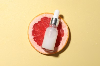 Photo of Bottle of cosmetic serum and grapefruit slice on wet yellow background, top view