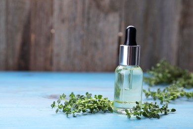 Photo of Bottle of thyme essential oil and fresh plant on light blue wooden table, space for text