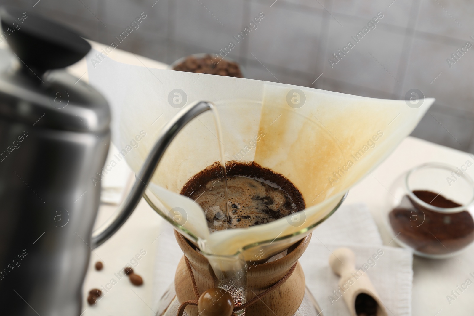 Photo of Making drip coffee. Pouring hot water into chemex coffeemaker with paper filter at table, closeup