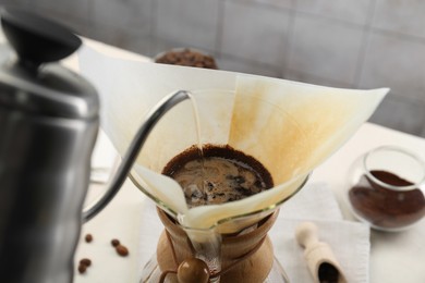 Photo of Making drip coffee. Pouring hot water into chemex coffeemaker with paper filter at table, closeup