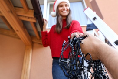 Photo of Woman and man decorating house with Christmas lights outdoors, selective focus