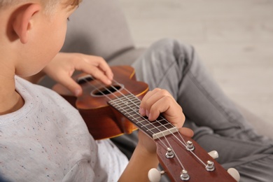 Photo of Little boy playing guitar on sofa in room, closeup