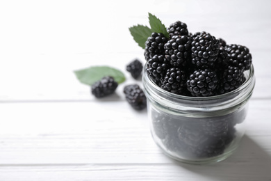 Photo of Fresh ripe blackberries in glass jar on white wooden table, closeup. Space for text