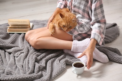 Photo of Woman with cute red cat and book on grey blanket at home, closeup view. Space for text