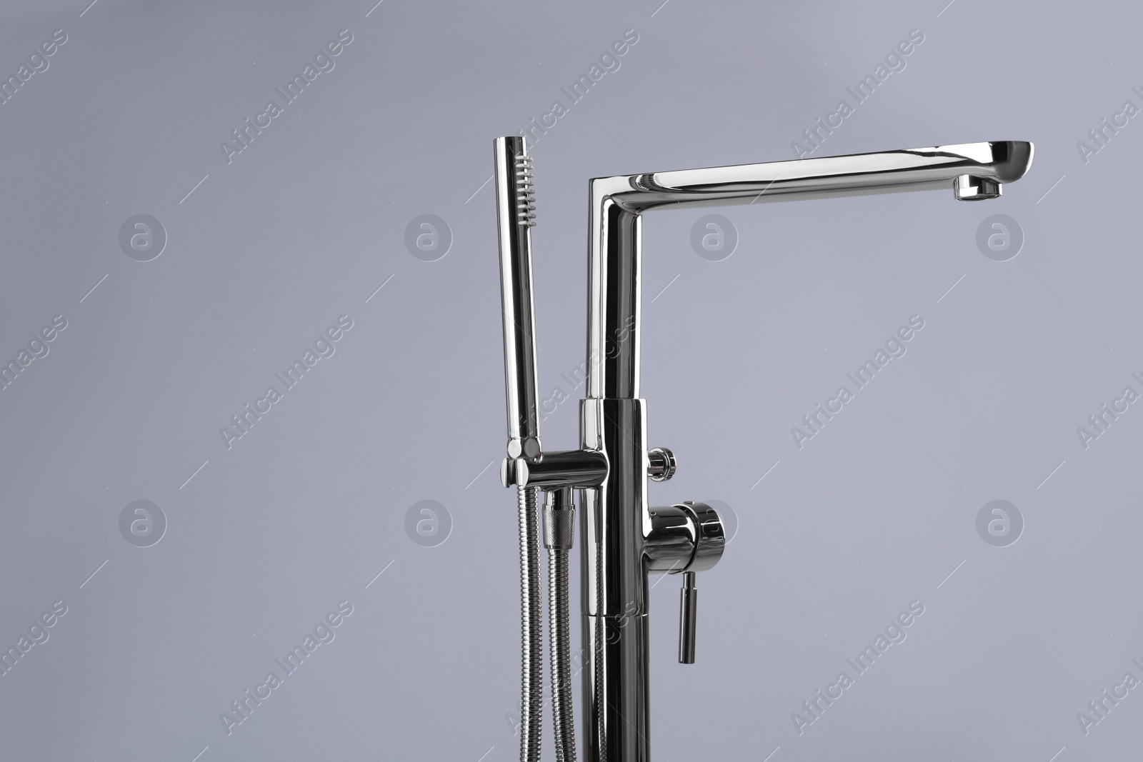 Photo of Modern bathtub faucet with hand shower on grey background